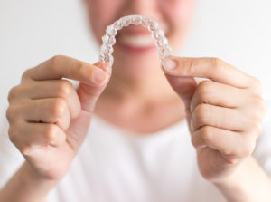 Smiling woman holding an Allen Invisalign clear aligner