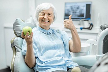 smiling woman with dentures in Allen, TX holding an apple